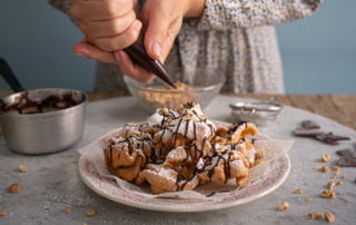 Fränkische Schneeballen con cioccolato fuso, zucchero a velo e granella di nocciole